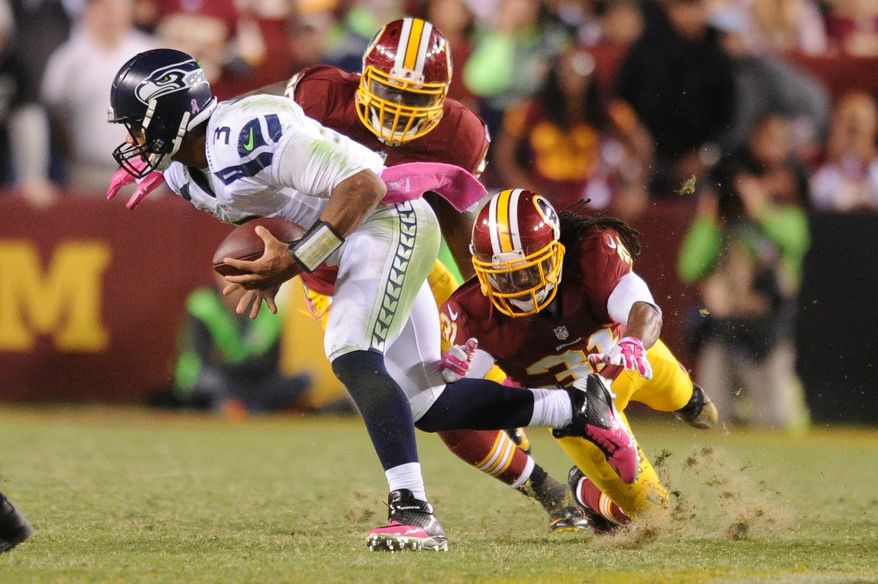 Seattle Seahawks quarterback Russell Wilson (3) eludes the sack from Washington Redskins strong safety Brandon Meriweather (31) and outside linebacker Brian Orakpo (98) during fourth quarter action at FedExField, Landover, Md., Oct. 6, 2014. (Preston Keres/Special for The Washington Times)
