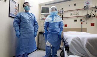 Bellevue Hospital nurse Belkys Fortune, left, and Teressa Celia, Associate Director of Infection Prevention and Control, pose in protective suits in an isolation room, in the Emergency Room of the hospital, during a demonstration of procedures for possible Ebola patients, Wednesday, Oct. 8, 2014. The U.S. government plans to begin taking the temperatures of travelers from West Africa arriving at five U.S. airports, including the New York area&#x27;s JFK International and Newark Liberty International, as part of a stepped-up response to the Ebola epidemic. (AP Photo/Richard Drew)