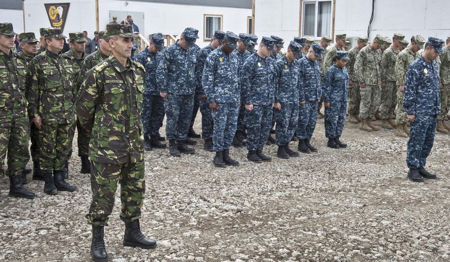 In this handout photograph from the US Navy, US service members deployed to the Naval Support Facility (NSF) Deveselu, groups center and right, bow their heads with members of the Romanian Military, left, during a religious moment of the establishment and assumption of command ceremony in Deveselu, Romania, Friday, Oct. 10, 2014. The NSF Deveselu Base, established more than 20 years ago, will be part of the Aegis Ballistic Missile Defense (BMD) System. The US Navy has taken control of a new missile defense base in southern Romania, one of two European land-based interceptor sites for a NATO missile shield which Russia strongly opposes.(AP Photo/U.S. Navy / LT j.g. Alexander Perrien, Handout)