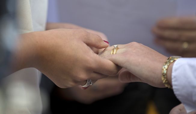 In this file photo, two women from Centreville, Va., hold hands after exchanging wedding rings during a ceremony in front of the Arlington County Courthouse in Arlington, Va., Monday, Oct. 6, 2014. A Virginia photographer, Chris Herring, is suing the state over a new law taking effect in July 2020. Mr. Herring says the law will infringe on his First Amendment rights by requiring him to promote same-sex weddings on his website. Mr. Herring has religious scruples that forbid him to photograph such ceremonies and argues in a court filing his free-speech rights are also infringed by the legislation. (AP Photo/Manuel Balce Ceneta) **FILE**
