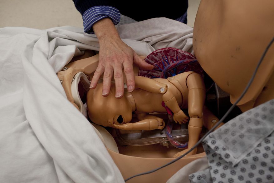 Theresa Atkinson, a mechanical engineering professor, places her hands on a model baby inside the stomach of Noelle, a robotic birthing stimulator, in a room at Kettering University in Flint, Mich., on Oct. 1, 2014. Noelle is used by engineering students to create tools for advancement in the medical field. (AP Photo/The Flint Journal, Laura McDermott ) LOCAL TELEVISION OUT; LOCAL INTERNET OUT