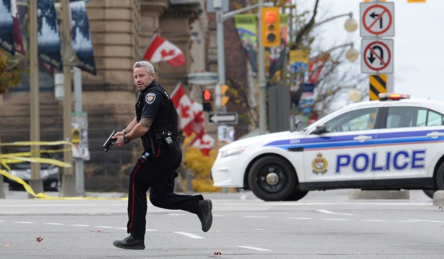 An Ottawa police officer runs with his weapon drawn outside Parliament Hill in Ottawa on Wednesday Oct. 22, 2014.  A soldier standing guard at the National War Memorial was shot by an unknown gunman and people reported hearing gunfire inside the halls of Parliament. Prime Minister Stephen Harper was rushed away from Parliament Hill to an undisclosed location, according to officials. (AP Photo/The Canadian Press, Sean Kilpatrick)