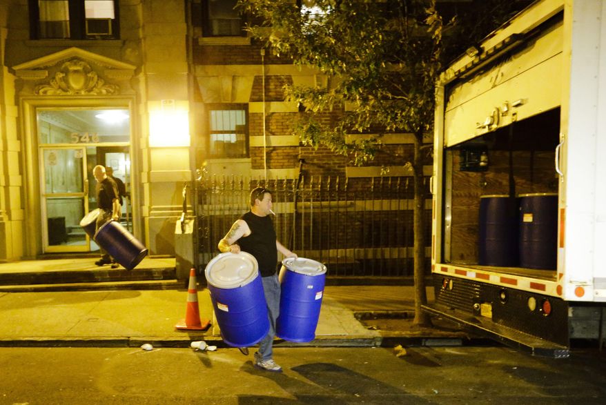Workers from BioRecoveryCorp carry barrels from the apartment building of Ebola patient Dr. Craig Spencer Friday, Oct. 24, 2014, in New York. Spencer remained in stable condition while isolated in a hospital, talking by cellphone to his family and assisting disease detectives who are accounting for his every movement since arriving in New York from Guinea via Europe on Oct. 17. (AP Photo/Frank Franklin II)