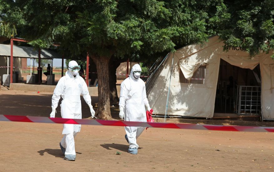 In this photo taken Saturday, Oct. 25, 2014, health workers walk towards an area used for Ebola quarantine after they worked with diseased Fanta Kone at a Ebola virus center in Kayes, Mali. After 2-year-old Fanta Kone’s father died in southern Guinea, the toddler’s grandmother took her from the forested hills where the Ebola outbreak first began months ago to bring her home to Mali. It wasn’t long, though, before the little girl started getting nosebleeds. (AP Photo/Baba Ahmed)