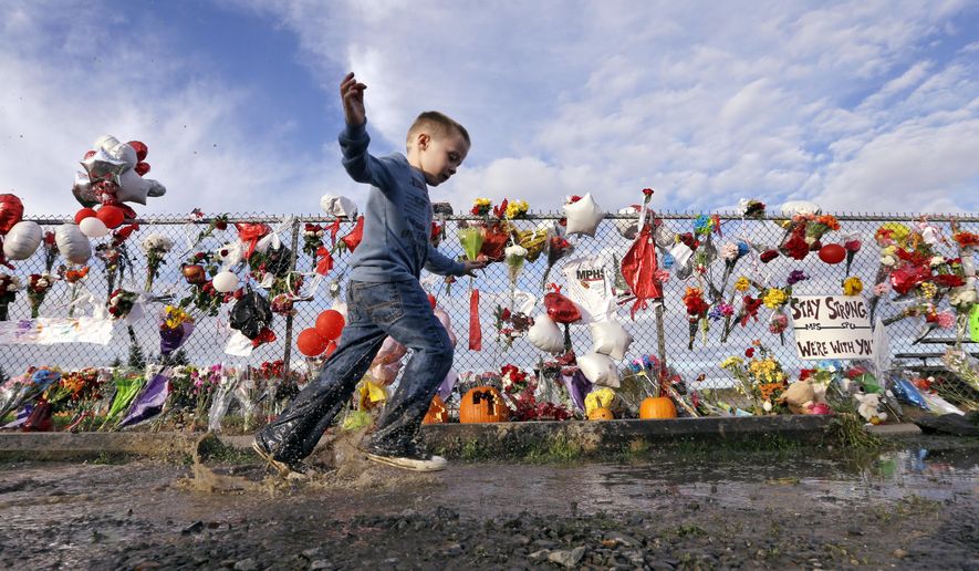 Jordan Wilmott, 4, races through a mud puddle in front of a fence at Marysville-Pilchuck High School covered with flowers, balloons and messages memorializing a shooting there last week, Wednesday, Oct. 29, 2014, in Marysville, Wash. Teacher Megan Silberberger who tried to intervene to stop the school shooting there last week says she reacted just as any of her colleagues would have. (AP Photo/Elaine Thompson)