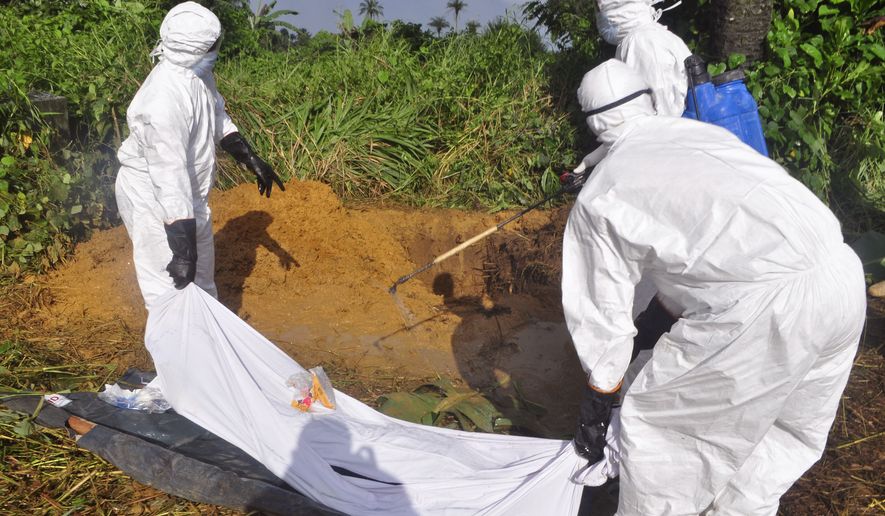 In this photo taken on Monday, Oct. 27, 2014. Health workers spray disinfectant on the body of a man as they prepare to place him into a grave, rear, as he is suspected of contracting and dying from the Ebola virus on the outskirts of Monrovia, Liberia. Liberia is making some progress in containing the Ebola outbreak while Sierra Leone is "in a crisis situation which is going to get worse," the top anti-Ebola officials in the two countries said. (AP Photo/Abbas Dulleh)