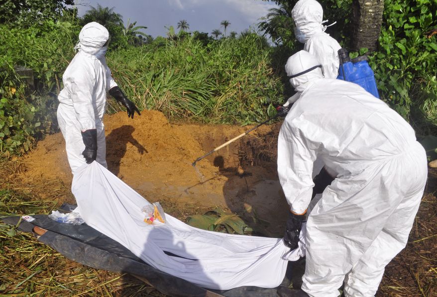 In this photo taken on Monday, Oct. 27, 2014. Health workers spray disinfectant on the body of a man as they prepare to place him into a grave, rear, as he is suspected of contracting and dying from the Ebola virus on the outskirts of Monrovia, Liberia. Liberia is making some progress in containing the Ebola outbreak while Sierra Leone is "in a crisis situation which is going to get worse," the top anti-Ebola officials in the two countries said. (AP Photo/Abbas Dulleh)