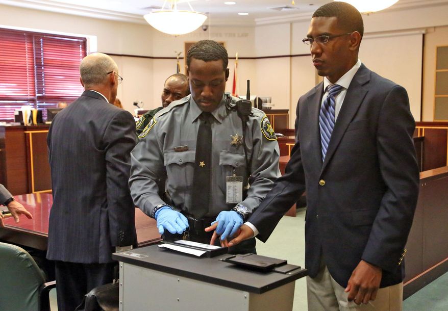Dante Martin, right, a former member of Florida A&M University's Marching 100 band looks at his family as he is fingerprinted Friday, Oct. 31, 2014, after being found guilty of manslaughter in the fatal hazing of drum major Robert Champion. Martin faces up to 22 years in prison, was found guilty of felony hazing and two misdemeanor counts of hazing involving two other band members. (AP Photo/Orlando Sentinel, Red Huber, Pool)