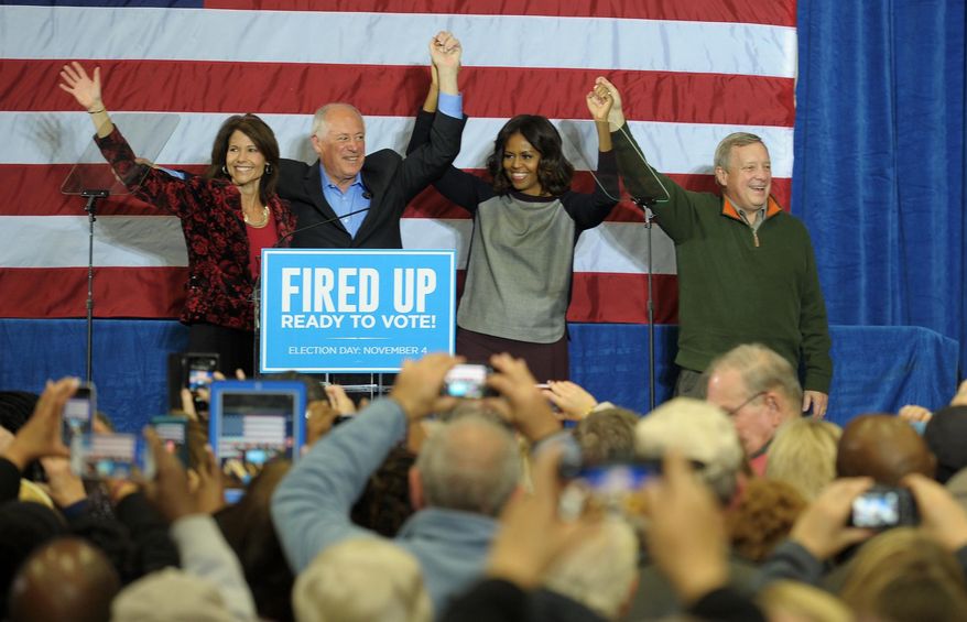First lady Michelle Obama holds hands during a rally for Illinois Democratic candidates Gov. Pat Quinn, second left, Sen. Dick Durbin, right, and Rep. Cheri Bustos, left, at Wharton Field House in Moline, Ill. on Saturday, Nov. 1, 2014. (AP Photo/The Dispatch, Todd Welvaert)