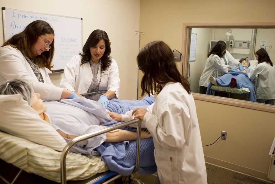 In this Oct. 23, 2014 photo, first year nursing students Kayleigh Mest, left, and Dana Kisiel, right, examine the SIM MAN during an exercise with their nursing instructor Julie Guernsey, center, at the Gillette College Health Science Education Center. Nursing students at Gillette College prepared for any and all threats, including Ebola, through training program. (AP Photo/Gillette News Record, Tim Goessman)