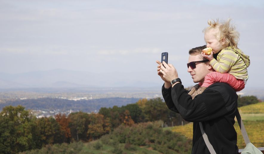 This Thursday, Oct. 30, 2014, photo shows Tom Patterson, 23, from Virginia Beach, and his 21-month-old daughter, Henley, enjoying the views from Carter Mountain Orchard in Charlottesville, Va. Dotted by charming small towns from the mountains to the west and the ocean to the east, Virginia is renewing efforts to tap its natural resources to help drive tourism. While summer remains the peak for tourism, state officials are working to shoulder the busier months with increased tourism other times of the year, especially fall, when leaves change from green to orange, yellow and red. (AP Photo/Michael Felberbaum)