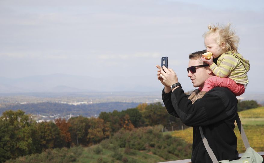 This Thursday, Oct. 30, 2014, photo shows Tom Patterson, 23, from Virginia Beach, and his 21-month-old daughter, Henley, enjoying the views from Carter Mountain Orchard in Charlottesville, Va. Dotted by charming small towns from the mountains to the west and the ocean to the east, Virginia is renewing efforts to tap its natural resources to help drive tourism. While summer remains the peak for tourism, state officials are working to shoulder the busier months with increased tourism other times of the year, especially fall, when leaves change from green to orange, yellow and red. (AP Photo/Michael Felberbaum)