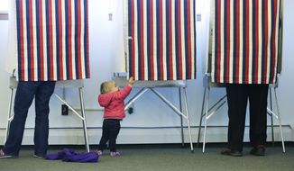 Zoe Buck, a 14-month-old child, checks out an empty voting booth as at her mother, Julie Buck, votes at left, Tuesday Nov. 4, 2014, at the Alaska Zoo polling place in Anchorage, Alaska. (AP Photo/Ted S. Warren)