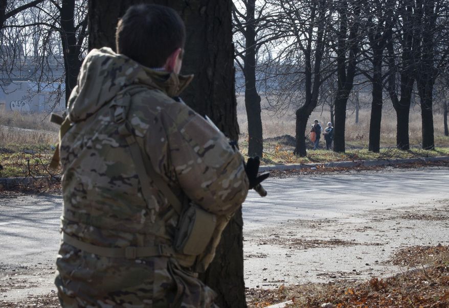 A pro-Russian rebel stands guard as women walk along a street not far from the front line near Donetsk airport in the city of Donetsk, eastern Ukraine Sunday, Nov. 2, 2014. The pro-Russian rebels are holding the elections that were dismissed by Ukraine and the West as illegitimate. (AP Photo/Dmitry Lovetsky)
