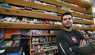 Brian Vincent poses in front of a large display of tobacco products at Vincent&#x27;s Country Store in Westminster, Mass., Thursday, Nov. 6, 2014. Local officials are contemplating what could be a first: a blanket ban on all forms of tobacco and e-cigarettes, leaving some shop owners fuming. (AP Photo/Elise Amendola)
