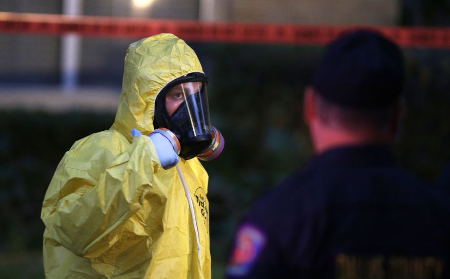 A hazmat worker looks up while finishing up cleaning outside an apartment building of a hospital worker Oct. 12 in Dallas. (Associated Press)