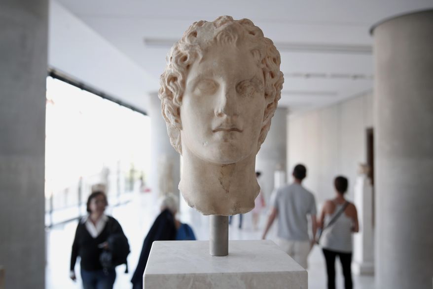 Visitors walk behind an ancient marble head of ancient Greek warrior-king Alexander the Great, displayed at the Acropolis museum in Athens, Oct. 12, 2014. Alexander the Great was one of the world&#x27;s most successful military commanders, who enlarged his father&#x27;s kingdom to include an empire stretching from modern Greece to India. During his youth, Alexander was tutored by the ancient Greek philosopher Aristotle until the age of 16. (AP Photo/Petros Giannakouris)