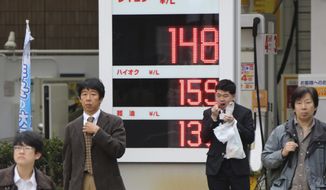 People wait to cross a street in front of a Shell filling station with the electric indicator showing a liter of regular gas price, top, at 148 yen, or $1.25, per liter (554 yen, or $4.69 per gallon) in Tokyo Friday, Nov. 28, 2014. A renewed plunge in oil prices is a worrying sign of weakness in the global economy that could shake governments dependent on oil revenues. It is also a panacea as pump prices fall, giving individuals more disposable income and lowering costs for many businesses. Partly because of the shale oil boom in the U.S., the world is awash in oil but demand from major economies is weak so prices are falling. The latest slide was triggered by OPEC’s decision Thursday to leave its production target at 30 million barrels a day. Member nations of the cartel are worried they’ll lose market share if they lower production. (AP Photo/Koji Sasahara)