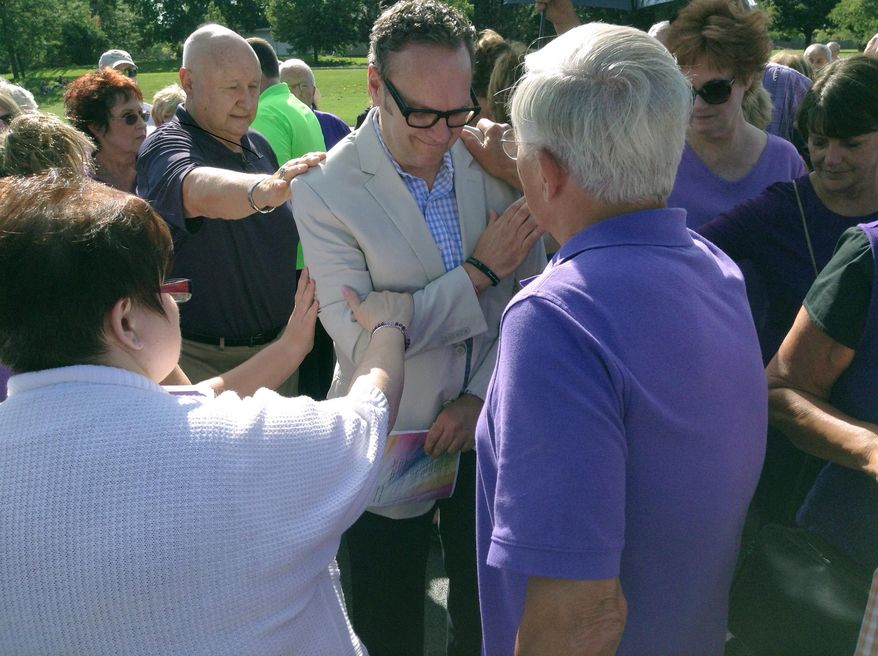 In this Sunday, Sept 7, 2014 photo, parishioners at Holy Family Parish in Inverness, Ill., place their hands on former music director Colin Collette as a symbol of support during a prayer vigil at the church Sunday. The longtime music director of a suburban Chicago parish has filed human rights complaints after he was fired earlier this year following his engagement to his same-sex partner. Collette, who worked at Holy Family Catholic Church in Inverness for 17 years, filed the complaints Thursday with the Chicago division of the Equal Employment Opportunity Commission and the Cook County Commission on Human Rights. (AP Photo/Daily Herald, Matt Arado)