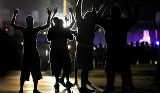 In this Aug. 11, 2014, file photo, people raise their hands in the middle of the street as police wearing riot gear move toward their position trying to get them to disperse, in Ferguson, Mo. (AP Photo/Jeff Roberson, File)