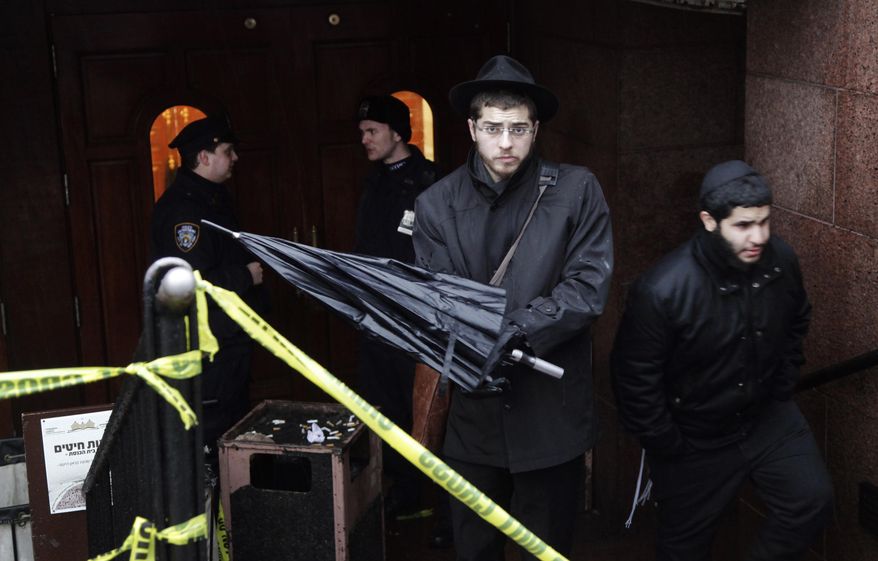 A member of the Lubavitch community, center, leaves the Chabad-Lubavitch Hasidic headquarters guarded by members of the New York Police Department, left, Tuesday, Dec. 9, 2014, in New York. A knife-wielding man stabbed an Israeli student inside the Brooklyn synagogue before being fatally shot by police after he refused to drop the knife. The student, Levi Rosenblatt, is in stable condition. (AP Photo/Mark Lennihan)
