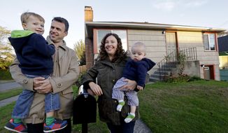 In this photo taken Wednesday, Oct. 15, 2014, Jennifer Ewing, second right, and her husband Florian Thiel pose for photos with their children Max, left, 3, and Felix, 8-months, outside their new home in Seattle’s Ballard neighborhood. The couple recently closed on the three-bedroom house , which cost slightly less than $500,000. They moved to Seattle from New York, another city that matches the pattern of high-income jobs and even more expensive housing. (AP Photo/Elaine Thompson)