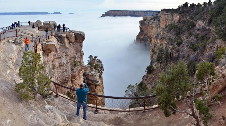 In this photo provided by the National Park Service, visitors to Mather Point on the South Rim of Grand Canyon National Park, in Ariz., view a rare weather phenomenon - a sea of thick clouds filling the canyon just below the rim, Thursday, Dec. 11, 2014. The total cloud inversion is expected to hang inside the canyon throughout Thursday. Cory Mottice of the National Weather Service said the weather event happens about once every several years, though the landmark was treated to one last year. (AP Photo/National Park Service, Michael Quinn)