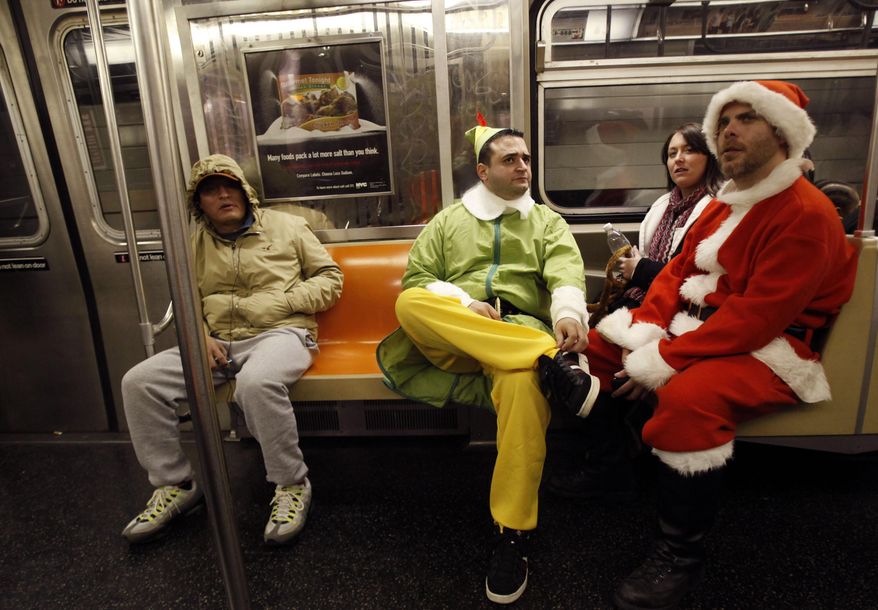 FILE- In this Dec. 11, 2010 file photo, SantaCon participants John Paul, center, dressed as an Elf and Michael Smallwood, dressed as Santa, ride the E train downtown New York. The annual event has faced mounting pressure from politicians, police and community groups as it grew from hundreds to thousands of costumed participants in roughly a decade. This year’s festivities fall on the same day as a planned march to protest recent killings of unarmed civilians by police. Santacon organizers are asking celebrants to keep their partying indoors (AP Photo/Mary Altaffer, File)