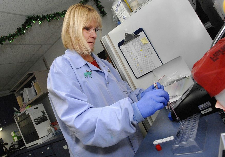 In this Dec. 11, 2014 photo taken in Normal, Ill., Sue Carroll, head of the microbiology section in the laboratory at Advocate BroMenn Regional Medical Center, drops a sample of patient fluids into a test tube before assessing the presence of flu virus using immunoflourescent technology. Seasonal flu is making an earlier appearance in Illinois this year and the most dominant strain seen in lab results is one that causes more severe illness. (AP Photo/The Pantagraph, David Proeber)