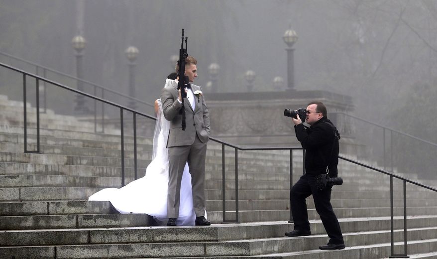 A groom holds an AR-10 rifle as he stands with his bride while the party was having their pre-wedding portraits taken on the steps of the capitol before a rally nearby by gun-rights advocates to protest a new expanded gun background check law in Washington state Saturday, Dec. 13, 2014, in Olympia, Wash. The wedding party was not part of the protest, but posed for pictures with it after being handed it by gun activist Brandon Lyons, who said "we've all just broken the law," by handing the gun over. Saturday's protest was called the "I Will Not Comply" rally, and those attending said they will openly exchange firearms in opposition to the state's new voter-approved universal background check law, Initiative 594. The law, which took effect on Dec. 4, requires background checks on all sales and transfers, including private transactions and many loans and gifts. (AP Photo/Elaine Thompson)