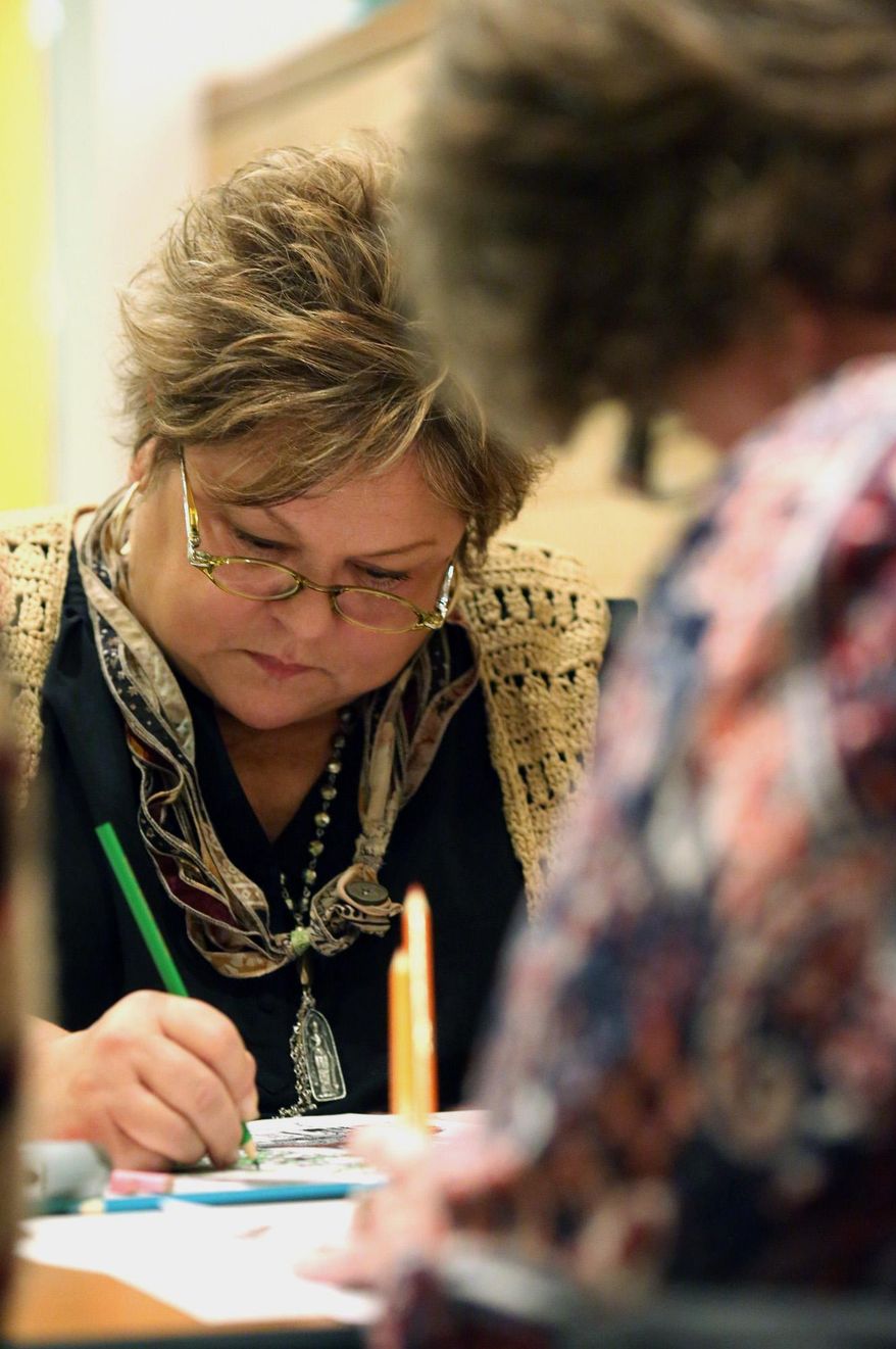 This photo taken Nov. 20, 2014, Diane Lazor focuses on a page during an adult coloring night at the Market 65 restaurant in Columbus, Ohio. The evening was created to promote "The Columbus Ohio Coloring and Activity Book" created by Katie Barron. The book features various Columbus scenes that encourage the artist to color in their own ideas about what shade the subject should be. The adult coloring nights allow guests to drink wine and talk while they color the pages. (AP Photo/The Columbus Dispatch, Brooke LaValley)