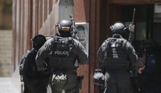 Armed police stand at the ready close to a cafe under siege at Martin Place in the central business district of Sydney, Australia, Monday, Dec. 15, 2014. A hostage situation erupted inside a chocolate shop and cafe in Australia&#39;s largest city on Monday, with the nation&#39;s prime minister saying it may be &quot;politically motivated.&quot; Television footage shot through the cafe&#39;s windows showed several people with their arms in the air and hands pressed against the glass, and two people holding up what appeared to be a black flag with white Arabic writing on it. (AP Photo/Rob Griffith)