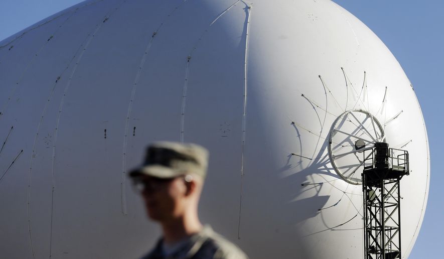 An unmanned aerostat that is part of a new U.S. military cruise-missile defense system floats over U.S. Army Capt. Jonathon Lewis during a media preview, Wednesday, Dec. 17, 2014, in Middle River, Md. Military officials said a pair of helium-filled aerostats stationed in Maryland are intended provide early detection of cruise missiles over a large swath of the East Coast, from Norfolk, Va., to upstate New York, during a three-year test. JLENS, short for Joint Land Attack Cruise Missile Defense Elevated Netted Sensor System, will be fully implemented this winter. (AP Photo/Patrick Semansky)