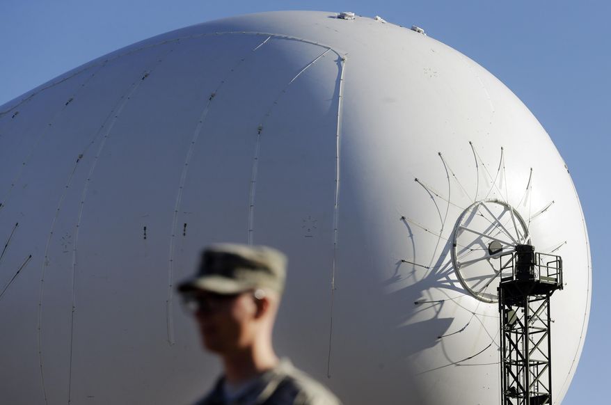 An unmanned aerostat that is part of a new U.S. military cruise-missile defense system floats over U.S. Army Capt. Jonathon Lewis during a media preview, Wednesday, Dec. 17, 2014, in Middle River, Md. Military officials said a pair of helium-filled aerostats stationed in Maryland are intended provide early detection of cruise missiles over a large swath of the East Coast, from Norfolk, Va., to upstate New York, during a three-year test. JLENS, short for Joint Land Attack Cruise Missile Defense Elevated Netted Sensor System, will be fully implemented this winter. (AP Photo/Patrick Semansky)