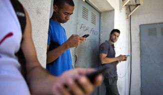 In this April 1, 2014 file photo, students stand outside a building to find an Internet signal for their phones in Havana, Cuba. (AP Photo/Ramon Espinosa, File)