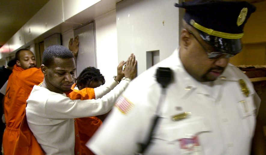 FILE PHOTO - Inmates Donnell Howard (foreground) and John Lawrence (background) wait handcuffed outside their cells while corrections officers search for contraband and weapons during a suprise search at the Washington DC Central Detention facility in Washington DC on Thursday, May 30, 2002.  The unannounced searches take place at least once a year and are planned so as to not allow inmates time to dispose of the weapons. Inmates are required to have paperwork for items such as authorized medication.  ( Gerald Herbert / The Washington Times ) 