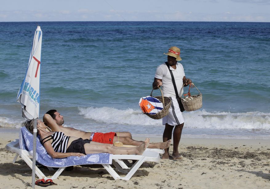 In this Dec. 19, 2014 photo, tourists sunbathe as a vendor sells kites decorated with Cuba's flag on a beach near Havana, Cuba. The easing of tourism regulations is a gamble for both the U.S. and Cuba. Obama said Wednesday that people-to-people travel was a way to “empower the Cuban people.” At the same time, a U.S. tourism surge could funnel sorely needed cash to a tourism industry run mostly by what Obama described Friday as “a regime that represses its people.” (AP Photo/Desmond Boylan)