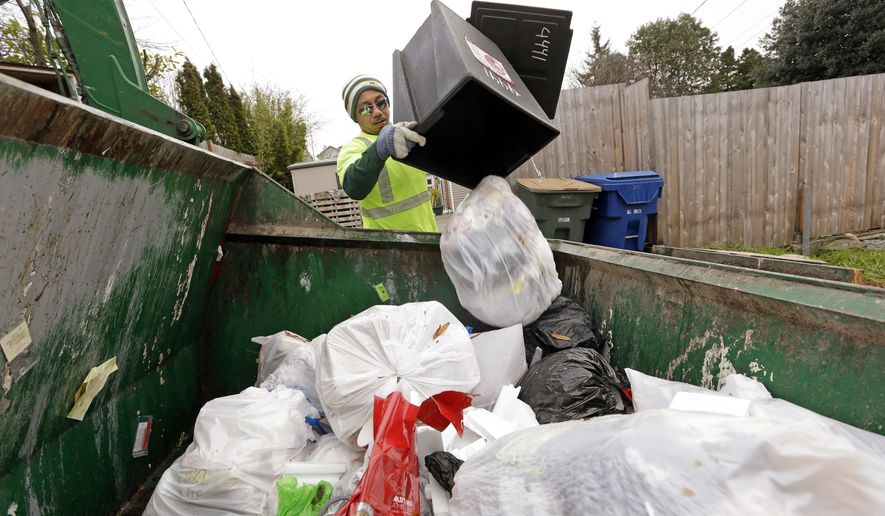 In this photo taken Monday, Dec. 22, 2014, garbage collector Anousone Sadettanh empties a small residential garbage bin into his truck as larger yard waste and recycling bins stand behind, in Seattle. Fail to recycle in Seattle and you can get a ticket from the garbage collector. The city says it will start enforcing new recycling requirements on Jan. 1 with warning tags. Careless residents will start seeing fines July 1 on their bills — $1 per violation, $50 for a commercial or apartment building. (AP Photo/Elaine Thompson)