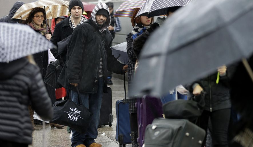 Travelers wait in the rain to board a bus for Washington, D.C. in New York, Wednesday, Dec. 24, 2014. Christmas Eve is shaping up to be windy, wet and warm instead of white across much of the country. (AP Photo/Seth Wenig)