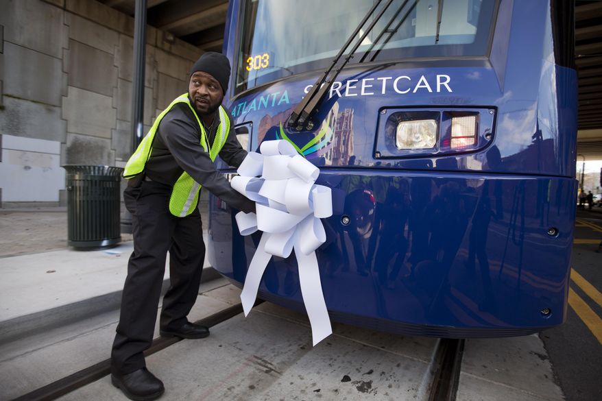 Operations and Maintenance Supervisor Darius Hall places a ribbon on an Atlanta Streetcar before it makes its inaugural trip through downtown, Tuesday, Dec. 30, 2014, in Atlanta. The inaugural journey marks the first time streetcars have regularly traversed Atlanta streets since 1949. The official launch of the new streetcar happened during a grand opening ceremony in Woodruff Park downtown, where dignitaries spoke, pastors blessed it with prayers and onlookers snapped photos on cellphones. (AP Photo/David Goldman)