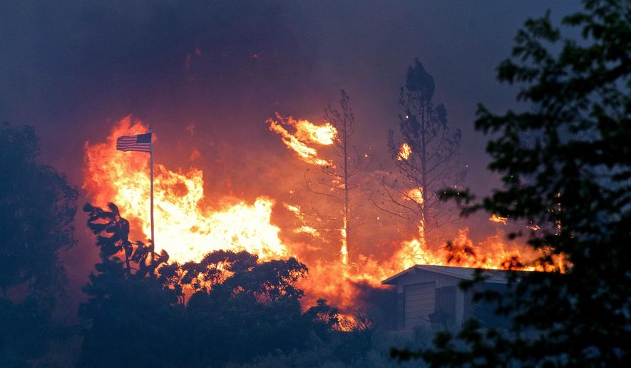 in this July 18, 2014, file photo, an American flag waves in the breeze as a wildfire approaches through trees in Malott, Wash. (AP Photo/The Spokesman-Review, Tyler Tjomsland, File)