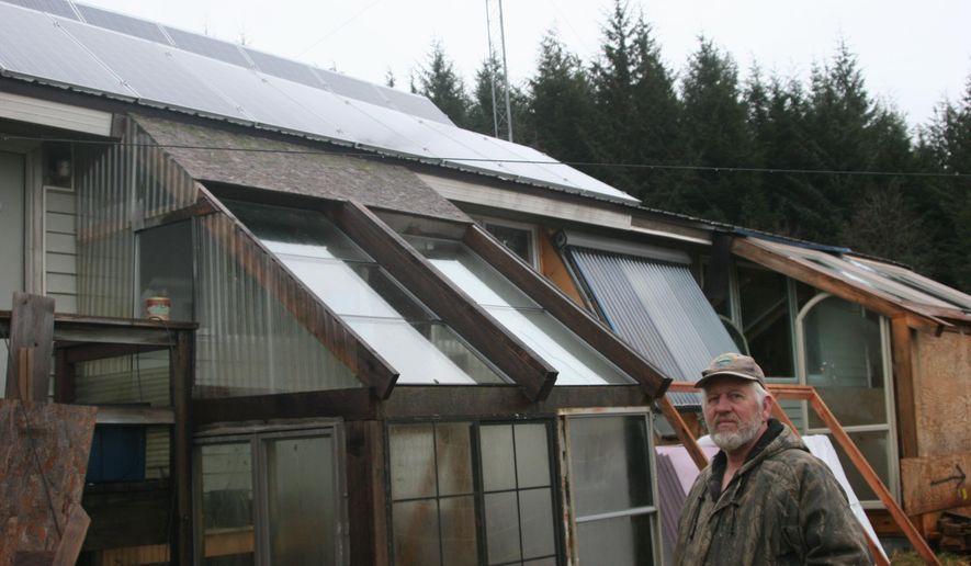 Elk Hunter stands Friday, Dec. 26, 2014, in front of his home in Kake, Alaska, where he installed 16 solar panels on his roof almost two years ago. (AP Photo/The Juneau Empire, Stephanie Shor)