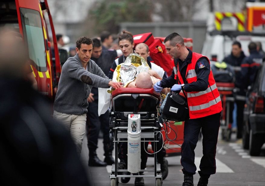 An injured person is whisked from the scene of deadly shootings at the offices of Charlie Hebdo, a Paris weekly. (Associated Press)