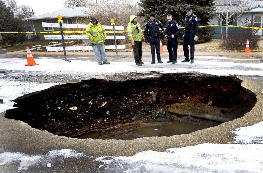 Members of Lafayette Public Works and the Lafayette Police Department look over a large sink hole on East Cleveland Street in Lafayette, Colo., Monday, Jan. 12, 2015. (AP Photo/Boulder Daily Camera, Mark Leffingwell)