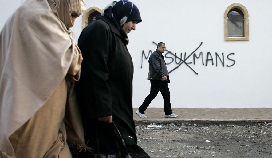 FILE - In this Monday Feb. 8, 2010 file photo, Muslim residents walk past racial slurs painted on the walls of a mosque in the town of Saint-Etienne, central France. Graffiti reads: "Muslims". Firebombs and pigs' heads are being tossed at mosques and women in veils have been insulted in a surge of anti-Muslim acts since last week's murderous assault on the newsroom of a satirical Paris paper, according to a Muslim who tracks such incidents in France. France's large Muslim population risks becoming collateral damage in the aftermath of the three attacks by French radical Islamists who killed 17 people. Muslims in other European countries also won't be spared, some Muslim leaders and experts say. Concern about a backlash against Muslims was discussed Monday Jan. 13, 2015, during a meeting on counter-terrorism measures at the Interior Ministry. (AP Photo/Laurent Cipriani, File)