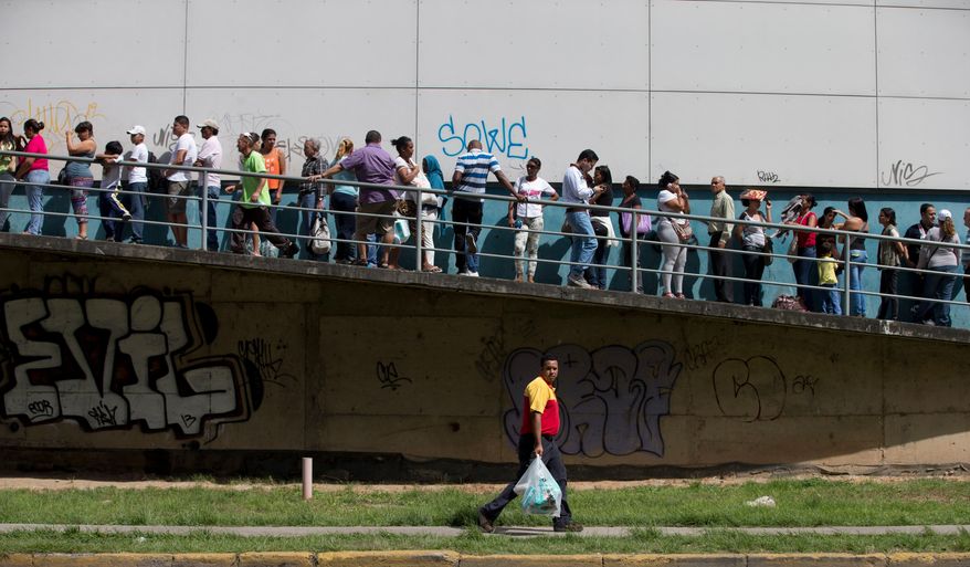 A man carries newly bought disposable diapers past a line of people waiting to enter a private supermarket to buy the same item in Caracas, Venezuela, Friday, Jan. 16, 2015. When Venezuelan President Nicolas Maduro returns from an urgent fundraising trip that has taken him to seven nations, so far, he’ll find his oil-dependent economy teetering on the edge and desperate countrymen searching empty store shelves for basic goods. (AP Photo/Fernando Llano)