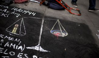A drawing asking for justice in Argentina, of the scales of justice, with a bullet on one side and blood on the other is seen on a sidewalk in Buenos Aires, Argentina, Tuesday, Jan. 20, 2015. Special prosecutor Alberto Nisman, who had been investigating the 1994 bombing of the AMIA Jewish community center in Buenos Aires that killed 85 people and who accused President Cristina Fernandez of shielding Iranian suspects, was found dead from a gun shot to the head in his apartment late Sunday, hours before he was to testify in a congressional hearing about the case. (AP Photo/Rodrigo Abd)