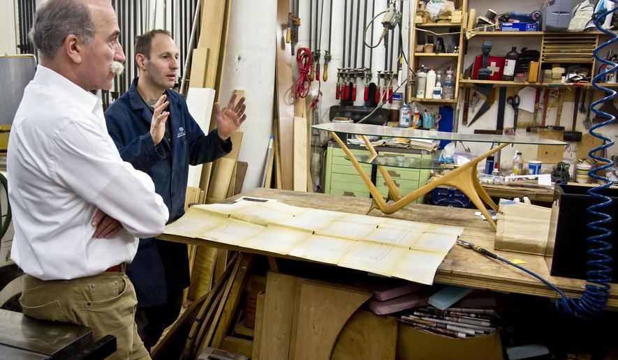 In this photo taken Thursday, Jan. 15, 2015, Miguel Saco, left, and Jean-Philippe Baty, a furniture maker, discuss work on a 1950s glass-and-oak coffee table by Italian architect and designer Carlo Mollino, at Miguel Saco Restoration Inc. in New York. Saco and his team of highly skilled artisans perform a wide range of museum-quality work, from the simplest cosmetic touch-ups and refinishing to caning, inlay, veneering, upholstery and recreation of missing parts. (AP Photo/Bebeto Matthews)