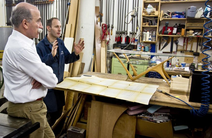 In this photo taken Thursday, Jan. 15, 2015, Miguel Saco, left, and Jean-Philippe Baty, a furniture maker, discuss work on a 1950s glass-and-oak coffee table by Italian architect and designer Carlo Mollino, at Miguel Saco Restoration Inc. in New York. Saco and his team of highly skilled artisans perform a wide range of museum-quality work, from the simplest cosmetic touch-ups and refinishing to caning, inlay, veneering, upholstery and recreation of missing parts. (AP Photo/Bebeto Matthews)