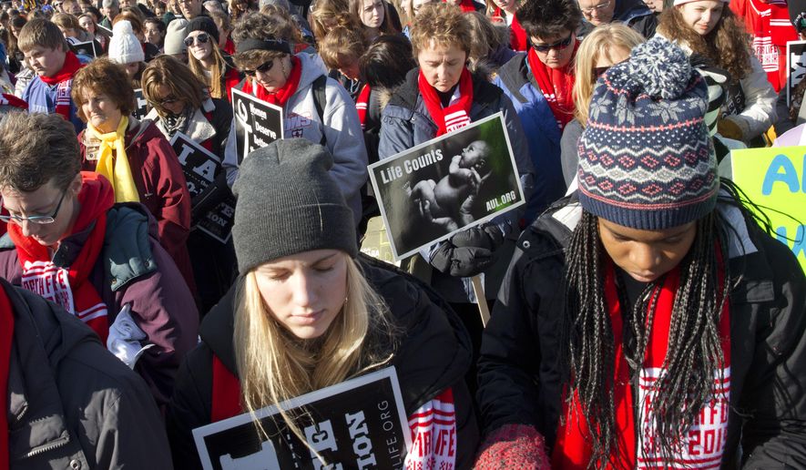 Lauren Sandy, 18, front left, and Afure Adah, 17, of Fargo, N.D., pray as they attend a pro-life rally at the annual March for Life, Thursday, Jan. 22, 2015, on the National Mall in Washington before marching to the Supreme Court. (AP Photo/Jacquelyn Martin)